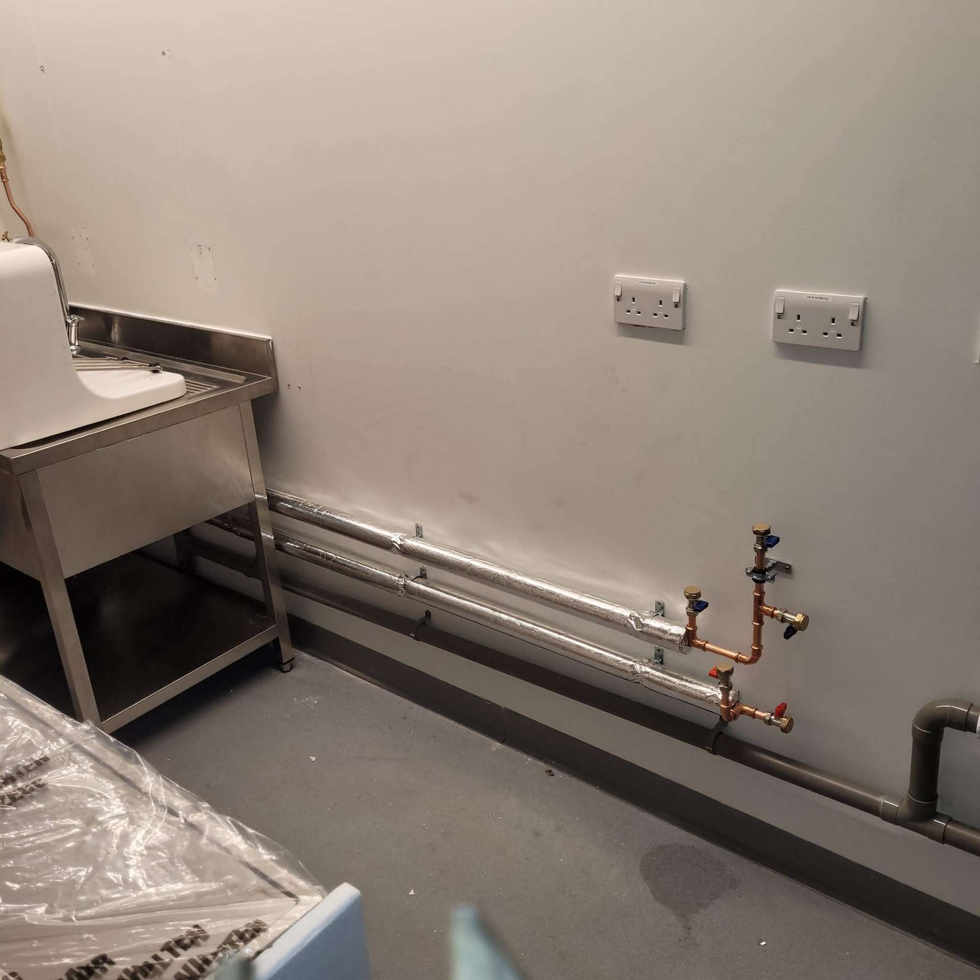 Commercial pipework first-fix run along skirting line in a fit-out project